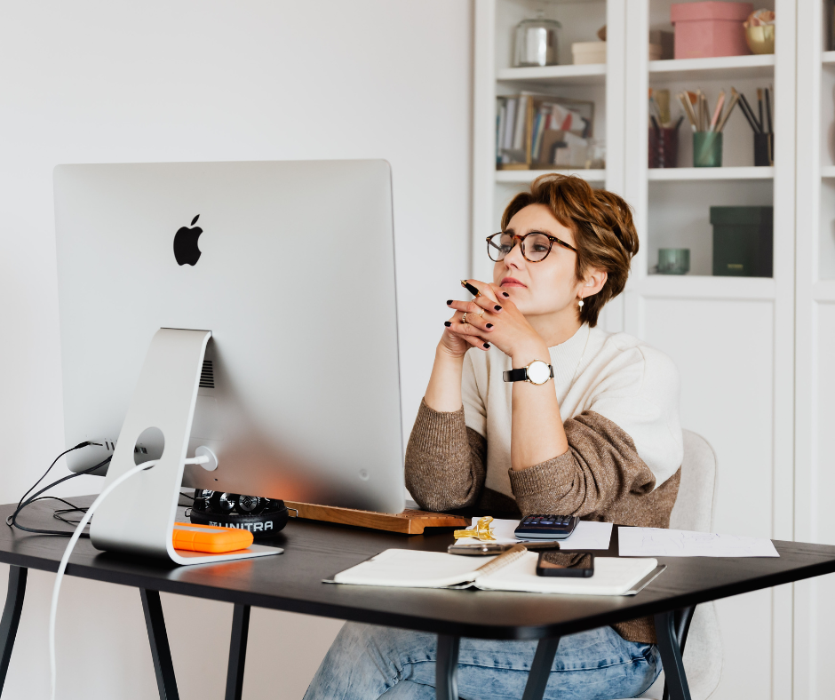 Woman sitting at desk with Mac computer contemplating